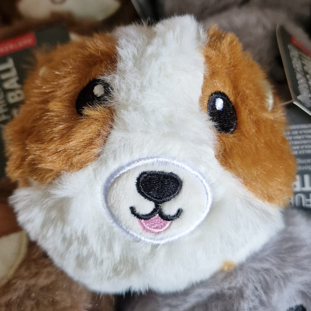 Plush toy stress ball with a dog face design among other plush toys in a box.