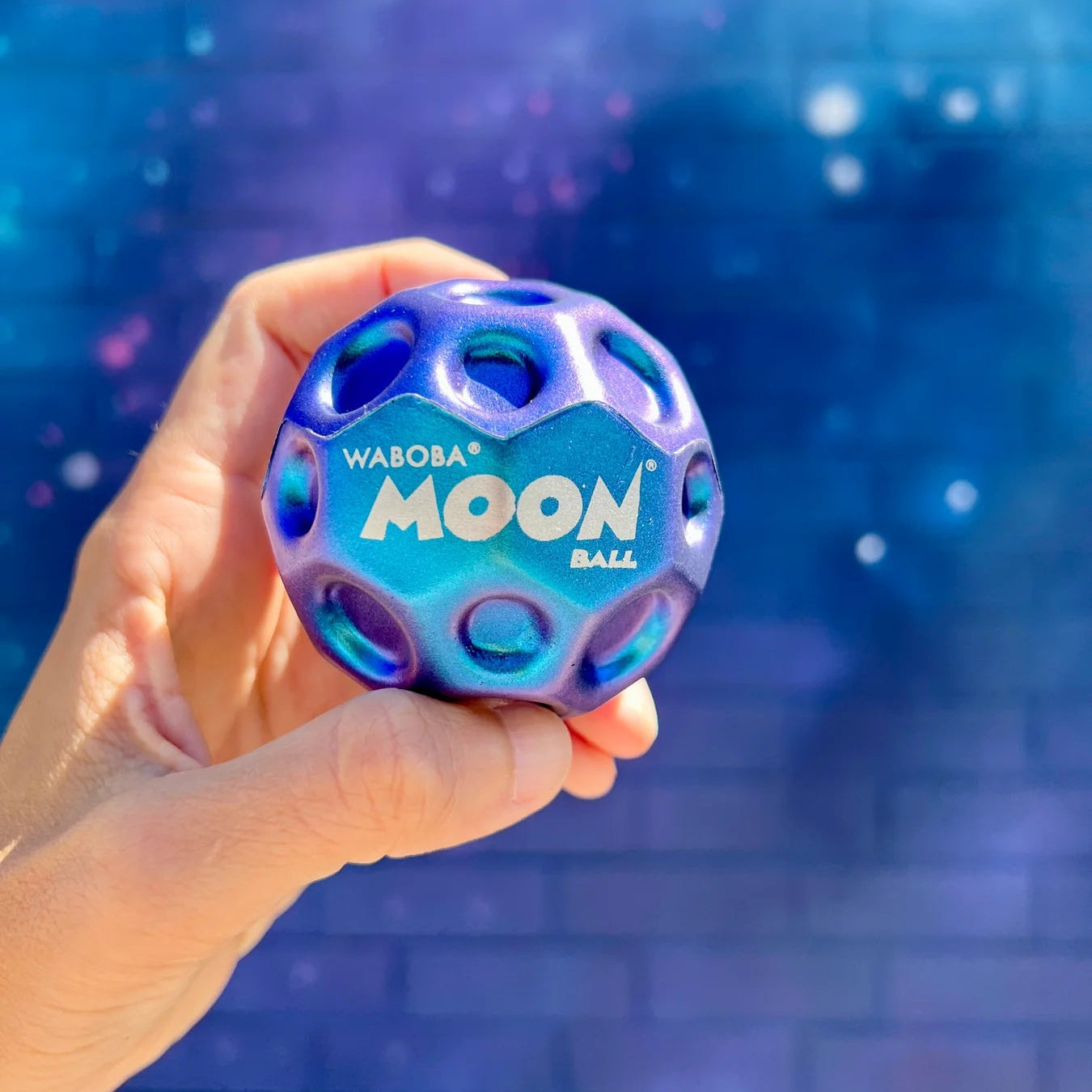 Hand holding a new metallic blue Waboba Moon ball against a blue water background